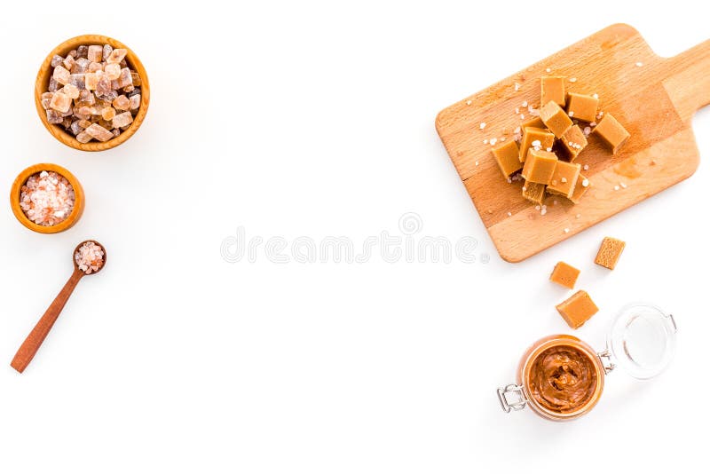 Cook caramel sauce. Melted caramel in glass jar, caramel cubes on cutting board, sugar and salt on white background top stock photo Cook caramel sauce. Melted caramel in glass jar, caramel cubes on cutting board, sugar and salt on white background top stock photo