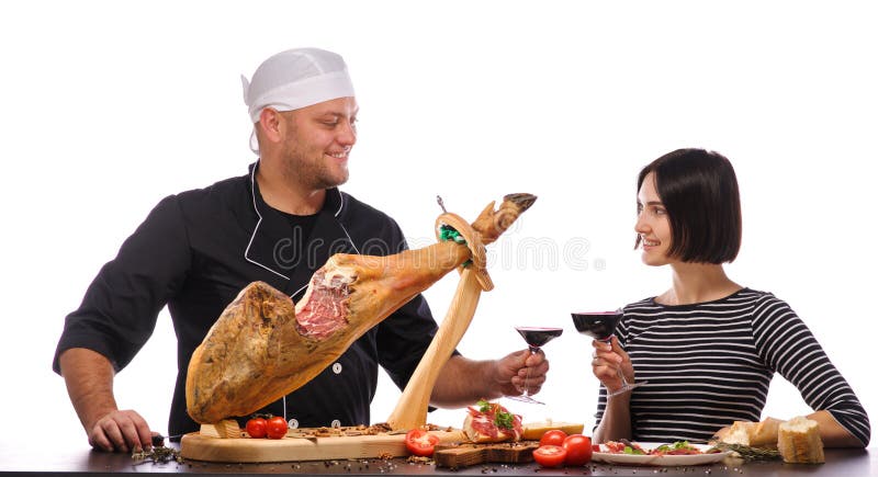 A cook with a girl is drinking wine near a whole jamon on a wooden stand. Isolated over white background