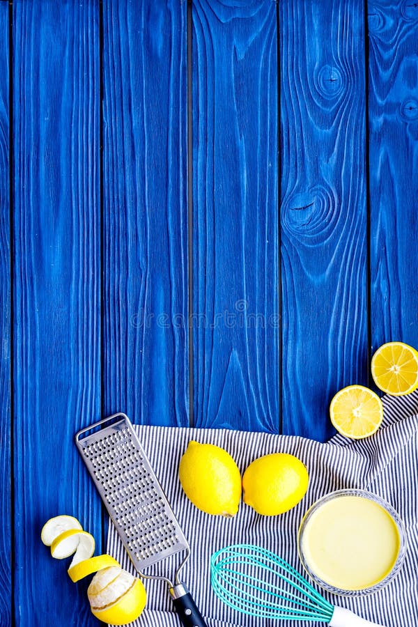 Cook lemon curd. Sweet cream in bowl, fruits, kitchen utensils grater and whisk on blue wooden background top view copy