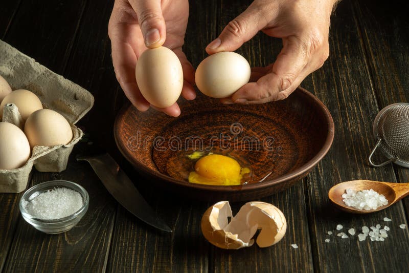 The cook prepares dinner with eggs. Close-up of a chef hands holding eggs over a plate royalty free stock images