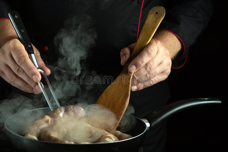 The cook prepares dinner in a frying pan. Frying meat sausage in the hotel kitchen stock images