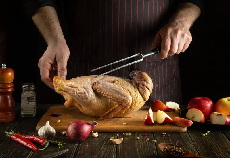 The cook prepares duck with apples on the kitchen table. Raw duck with apples and spices on a cutting board. Fork in the chef hand royalty free stock photos