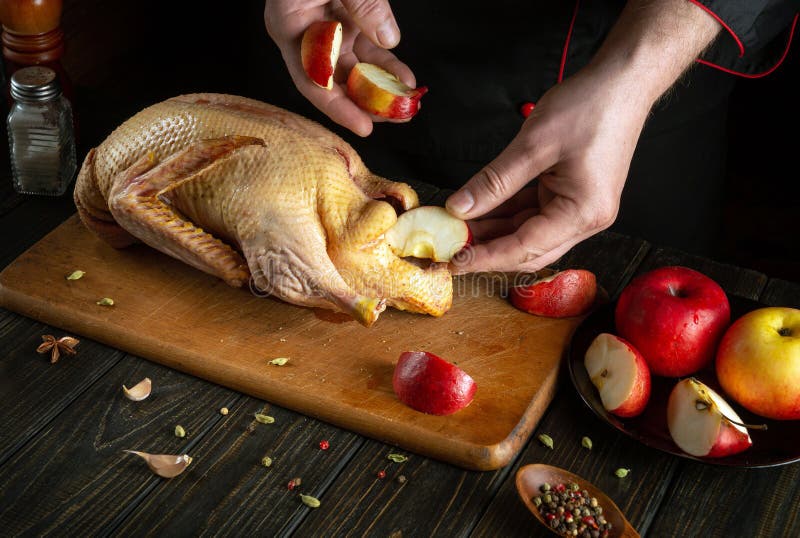 The cook prepares a duck for roasting with apples in the oven. Raw duck on a kitchen cutting board stock photo