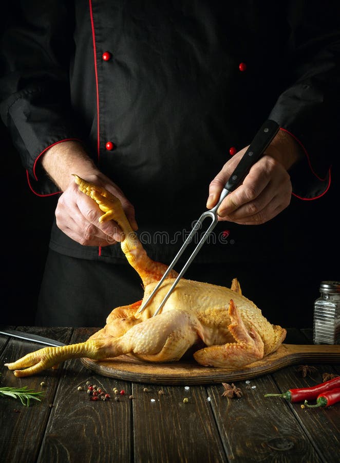 The cook prepares raw rooster on the kitchen table. Raw chicken on a cutting board before baking. Fork in the chef hand stock images