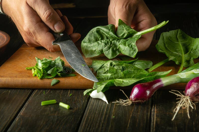 The cook prepares a salad with spinach and vegetables on the kitchen table. The concept of cooking vegetable salad for a royalty free stock image