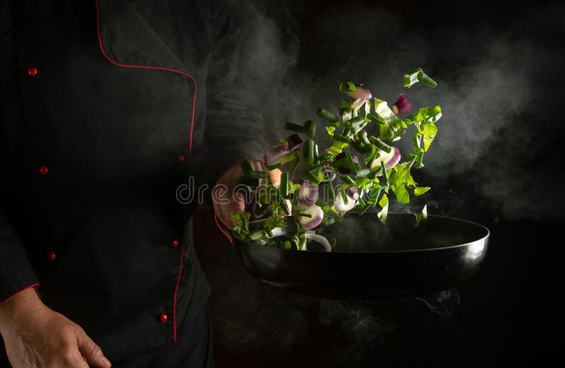 The cook prepares vegetables in a frying pan. The concept of preparing a vegetarian dish in the restaurant kitchen stock photo
