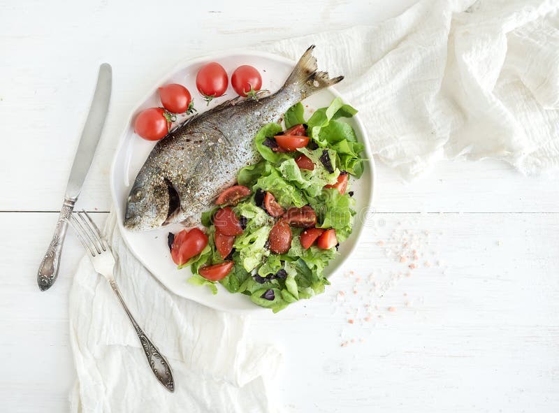 Cooked sea bream fish with fresh vegetable salad.