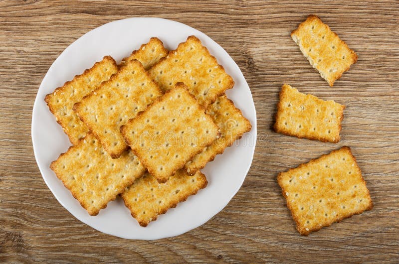 Cookies with sesame in plate, broken cracker on wooden table. Top view