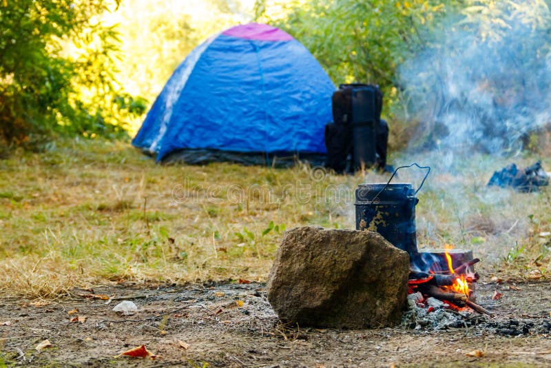Cooking on Campfire in Camping. Tent and Backpack on Background Stock