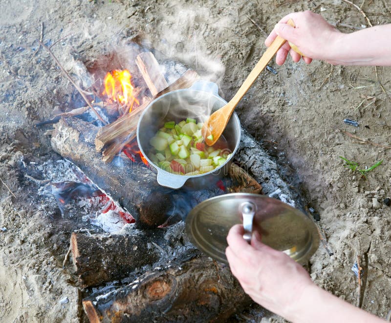 Cooking on campfire at picnic, food prepared in pot on wood, potatoes and tomatoes, healthy vegetarian food, woman hands with stock photography Cooking on campfire at picnic, food prepared in pot on wood, potatoes and tomatoes, healthy vegetarian food, woman hands with stock photography