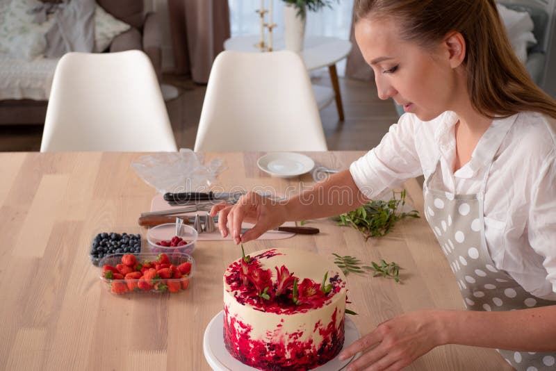 Cooking and decoration of cake with cream. Young woman pastry chef in the kitchen decorating red velvet cake