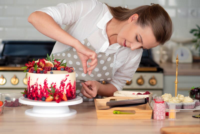 Cooking and decoration of cake with cream. Young woman pastry chef in the kitchen decorating red velvet cake