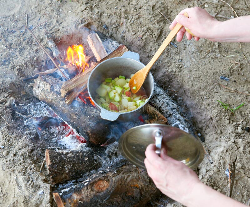 Cooking on fire at picnic, food prepared in pot on wood, potatoes and tomatoes, healthy vegetarian food, woman hands with spoon royalty free stock image Cooking on fire at picnic, food prepared in pot on wood, potatoes and tomatoes, healthy vegetarian food, woman hands with spoon royalty free stock image