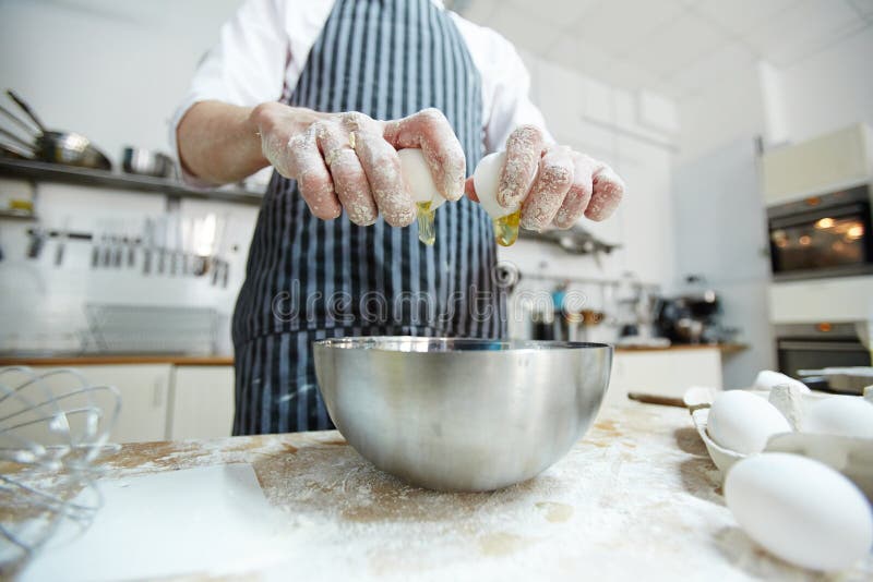 Pastry chef breaking egg into bowl in process of preparing dough for homemade buns during master-class. Pastry chef breaking egg into bowl in process of preparing dough for homemade buns during master-class