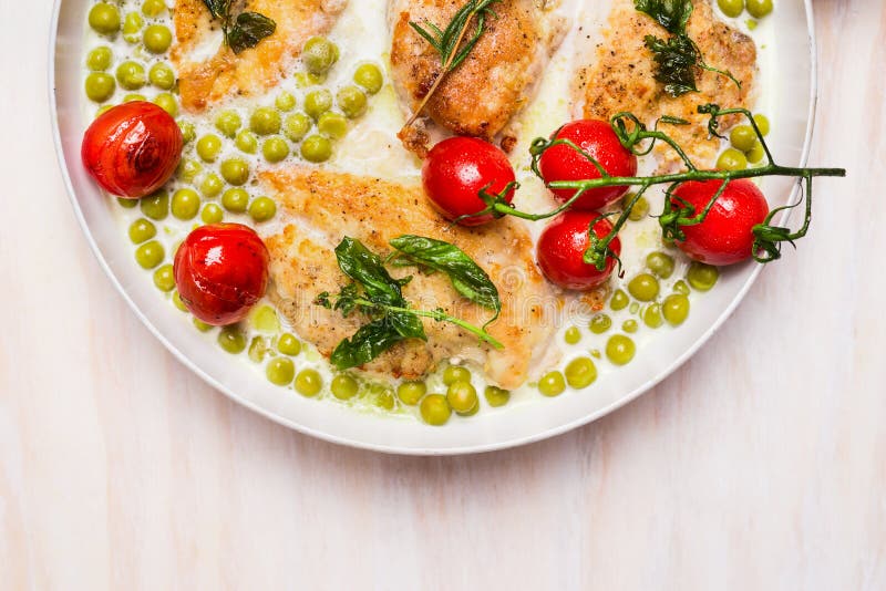 Cooking pan with chicken breast , green pea and roast tomatoes in cream sauce on wooden background, top view