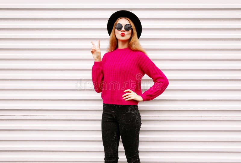 cool cheerful girl blowing red lips sending sweet air kiss in colorful pink knitted sweater, black round hat stock photo cool cheerful girl blowing red lips sending sweet air kiss in colorful pink knitted sweater, black round hat stock photo