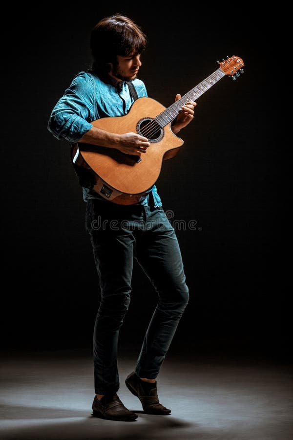 Cool guy standing with guitar on dark background