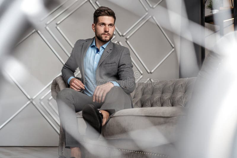 Cool and handsome. Good looking young man in full suit sitting on the sofa while spending time indoors. stock images Cool and handsome. Good looking young man in full suit sitting on the sofa while spending time indoors. stock images
