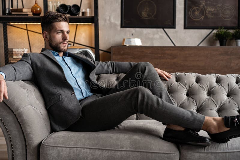 Cool and handsome. Good looking young man in full suit sitting on the sofa while spending time indoors. stock images Cool and handsome. Good looking young man in full suit sitting on the sofa while spending time indoors. stock images