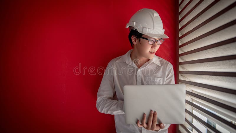 Coordenador masculino asiático com o capacete que trabalha com portátil imagens de stock Coordenador masculino asiático com o capacete que trabalha com portátil imagens de stock