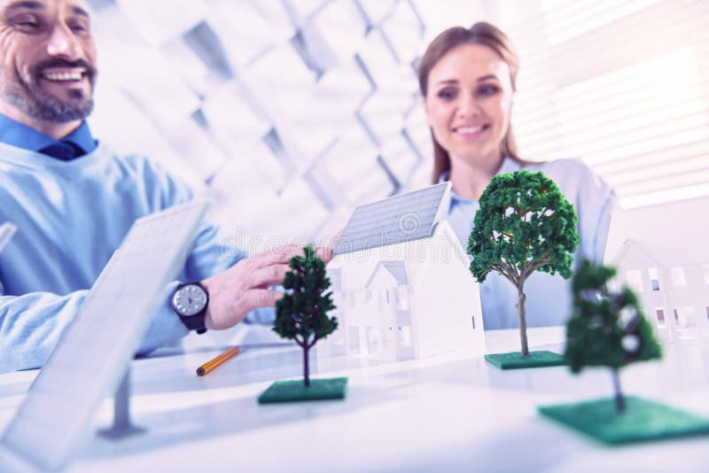 Coordenador positivo do eco que sorri ao colocar a bateria solar na miniatura da casa imagens de stock Coordenador positivo do eco que sorri ao colocar a bateria solar na miniatura da casa imagens de stock