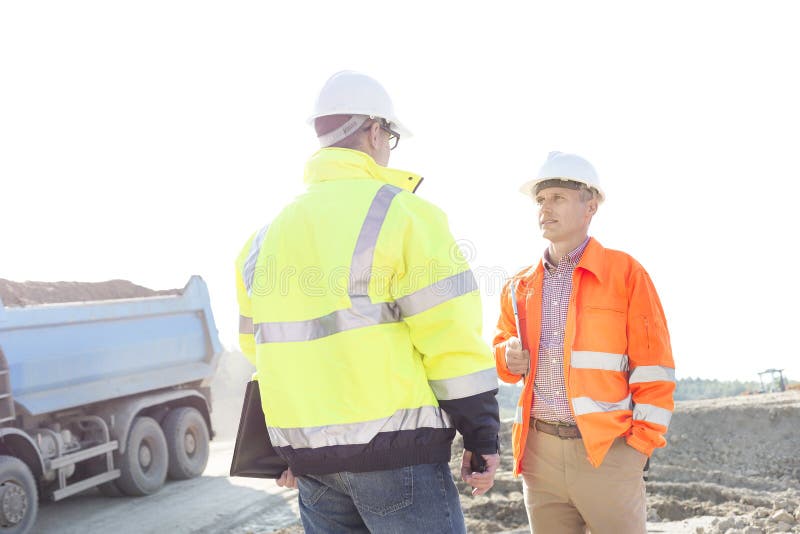 Coordenadores que discutem no canteiro de obras contra o céu claro no dia ensolarado fotografia de stock Coordenadores que discutem no canteiro de obras contra o céu claro no dia ensolarado fotografia de stock