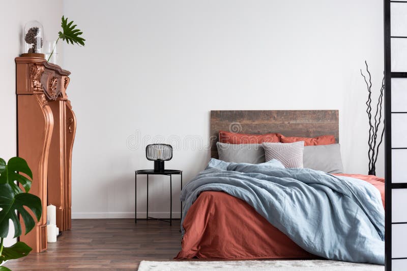 Copiare spazio su una parete bianca vuota della camera da letto rustica con un letto grande con una lettiera arancione e blu paste fotografia stock