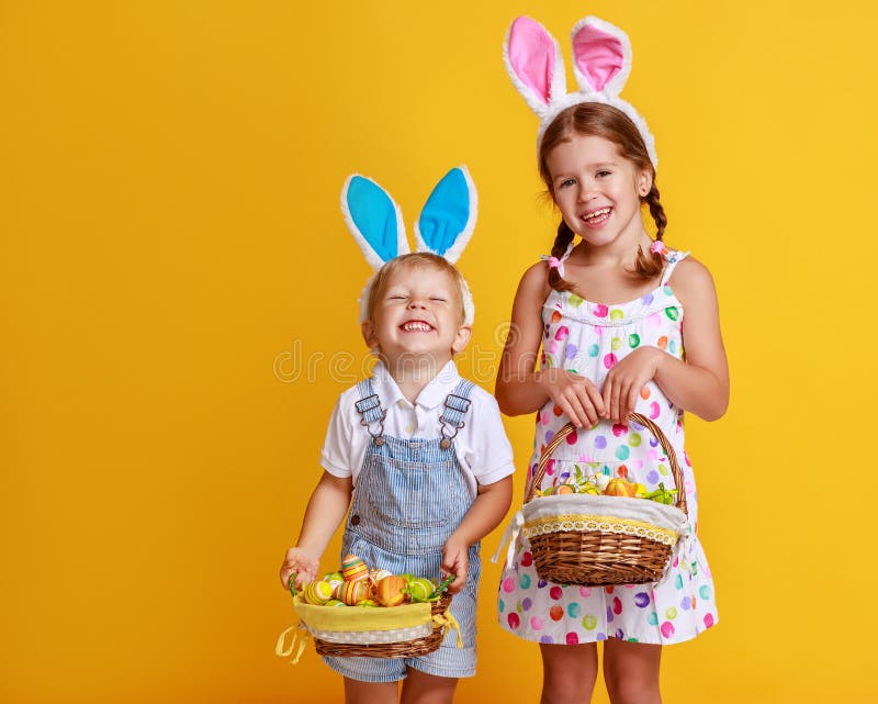 Copii amuzanți fericiți cu ouă de Paști și urechi de Iepuri pe galben stock images