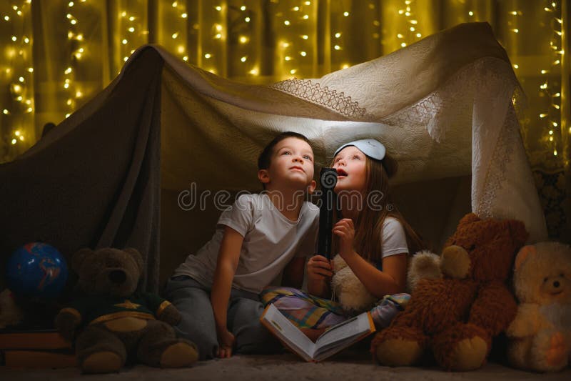 Copii, băieți și fete jucându-se și speriindu-se unul pe celălalt cu lanternă în cort noaptea stock photography