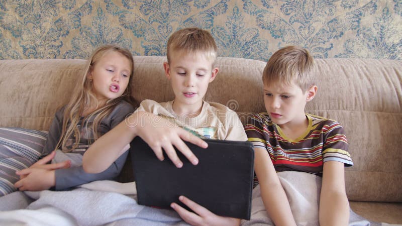 Copiii care se joacă pe tabletă acasă și stau pe canapea stock footage