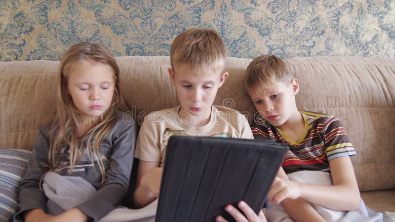 Copiii care se joacă pe tabletă acasă și stau pe canapea stock footage