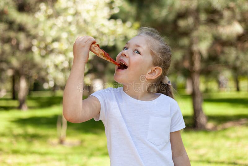 Copilul mănâncă o felie de pizza. fata din parc la un picnic. delicioasă mâncare de pe stradă royalty free stock photos