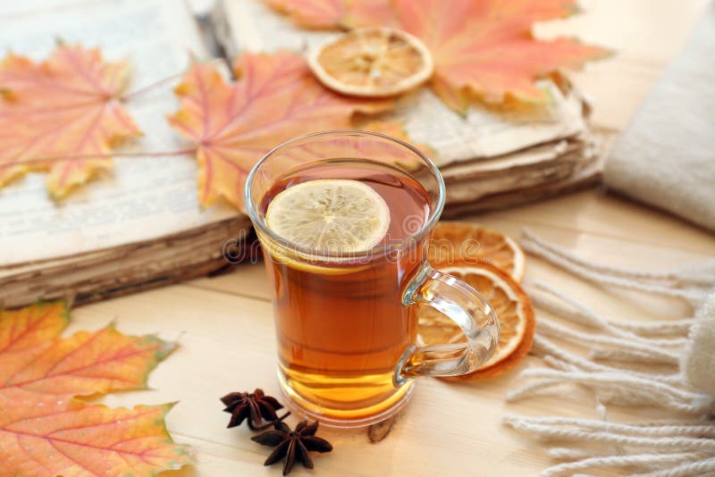Copo de vidro do chá aromático com folhas e livro de outono na tabela de madeira imagem de stock Copo de vidro do chá aromático com folhas e livro de outono na tabela de madeira imagem de stock