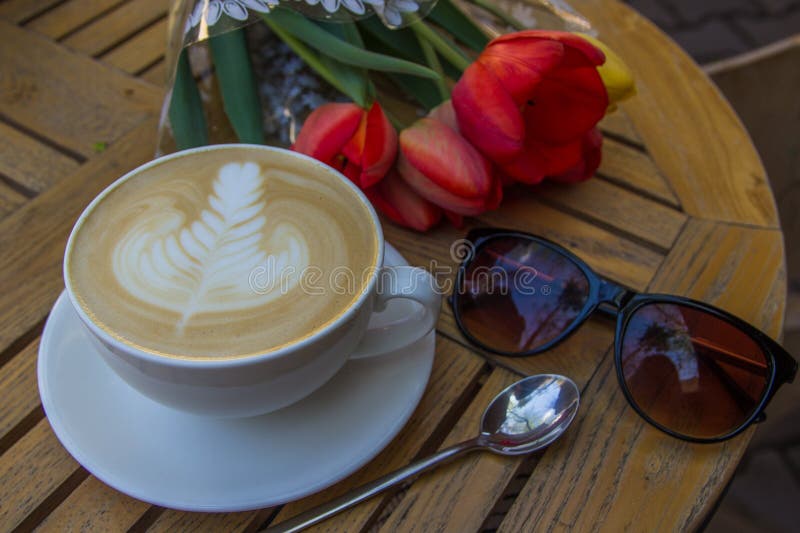 Copo do café, de vidros e de tulipas quentes da arte do latte na tabela de madeira fotografia de stock Copo do café, de vidros e de tulipas quentes da arte do latte na tabela de madeira fotografia de stock