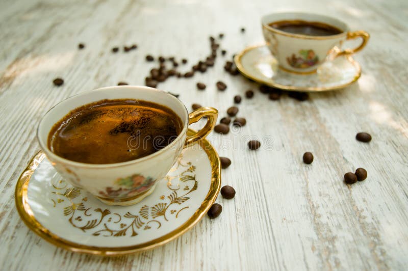 Two golden coffee cups on the white table with coffee yield scattered around Black coffee. Two golden coffee cups on the white table with coffee yield scattered around Black coffee.