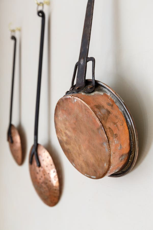 Copper Pots and Kitchen Utinsils Hanging on a White Painted Wall Stock