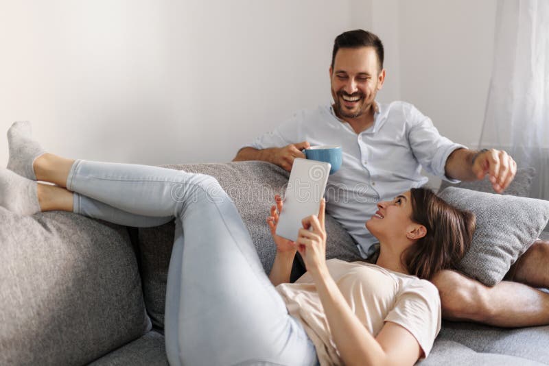 Beautiful young couple in love relaxing at home, drinking coffee and surfing the Internet using tablet computer. Beautiful young couple in love relaxing at home, drinking coffee and surfing the Internet using tablet computer