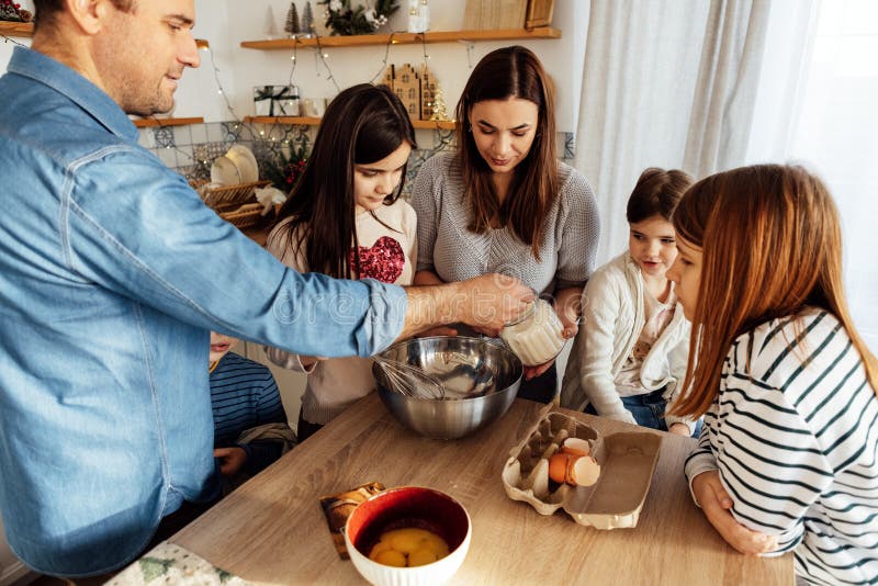 Coppia di allegri sposati e i loro bambini carini cucinano insieme in cucina a casa. il giovane aggiunge zucchero alla ciotola. fr immagini stock libere da diritti