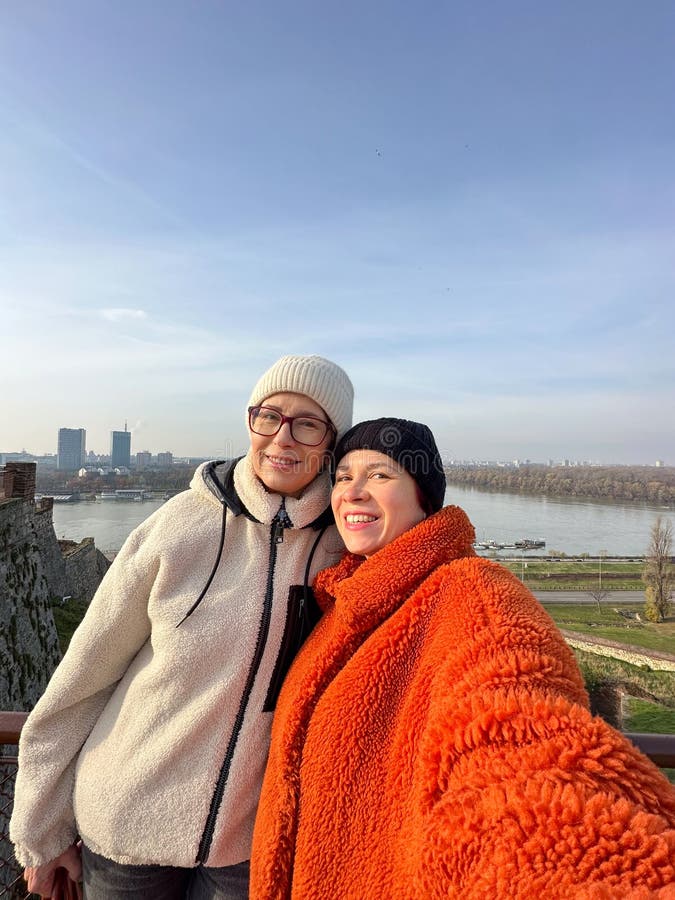 Coppia di gioielli, madre e figlia si fanno un selfie sullo sfondo di un fiume scenico in abiti caldi d'autunno e felici fotografia stock libera da diritti