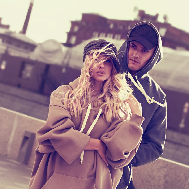 Coppia di stilliani che cammina in camicie magre moderne e cappelli alla moda sullo sfondo degli edifici della città autunnale immagini stock libere da diritti Coppia di stilliani che cammina in camicie magre moderne e cappelli alla moda sullo sfondo degli edifici della città autunnale immagini stock libere da diritti