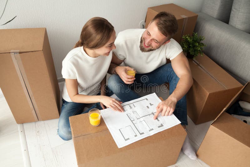Coppia la discussione della pianta della casa che si siede sul pavimento con le scatole commoventi fotografia stock libera da diritti Coppia la discussione della pianta della casa che si siede sul pavimento con le scatole commoventi fotografia stock libera da diritti