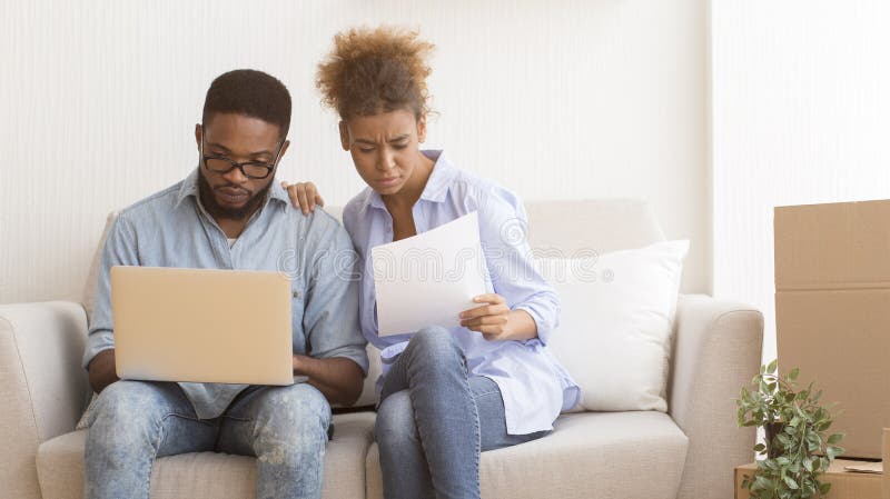 Coppie Afro Che Utilizzano Documenti Di Proprietà Di Lettura Laptop Seduti Sul Divano fotografia stock Coppie Afro Che Utilizzano Documenti Di Proprietà Di Lettura Laptop Seduti Sul Divano fotografia stock