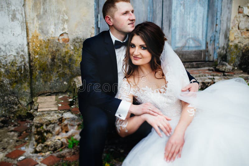 Coppie alla moda di nozze che si siedono vicino alla vecchia casa fotografia stock libera da diritti Coppie alla moda di nozze che si siedono vicino alla vecchia casa fotografia stock libera da diritti