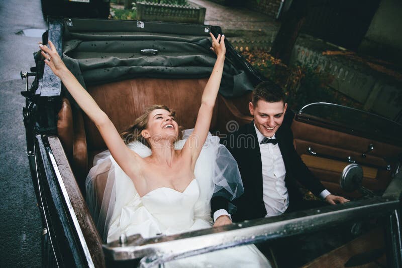 Coppie alla moda felici della persona appena sposata che posano in una retro automobile immagini stock libere da diritti Coppie alla moda felici della persona appena sposata che posano in una retro automobile immagini stock libere da diritti