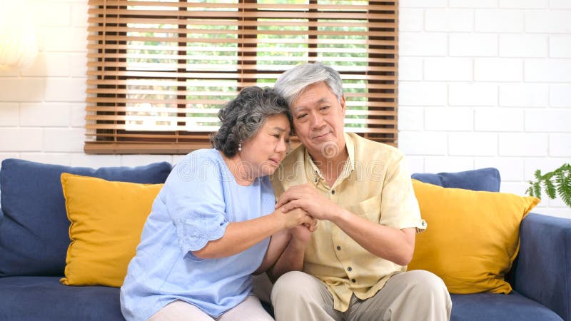 Coppie asiatiche senior che si confortano da emozione depressa mentre sedendosi sul salone del sofà a casa, vecchio pensionamento fotografia stock libera da diritti Coppie asiatiche senior che si confortano da emozione depressa mentre sedendosi sul salone del sofà a casa, vecchio pensionamento fotografia stock libera da diritti