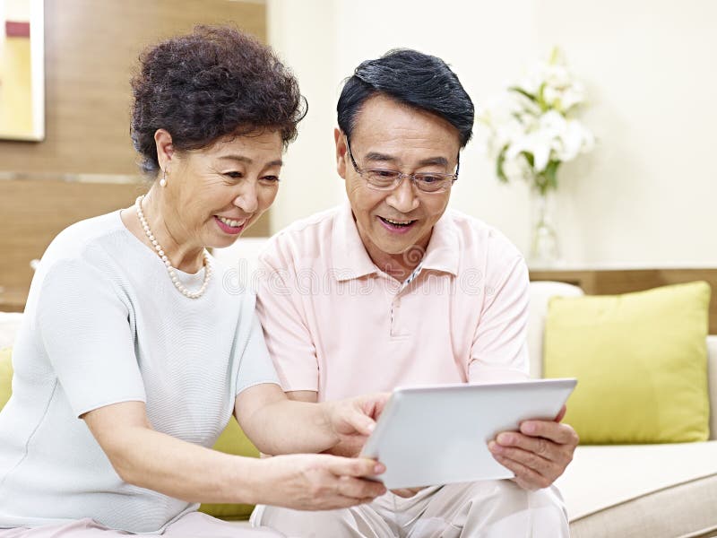 Senior asian couple sitting on couch looking at tablet computer together, happy and smiling. Senior asian couple sitting on couch looking at tablet computer together, happy and smiling