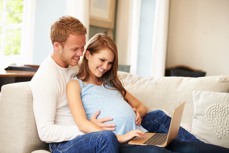 Coppie con la donna incinta che per mezzo insieme del computer portatile fotografie stock Coppie con la donna incinta che per mezzo insieme del computer portatile fotografie stock