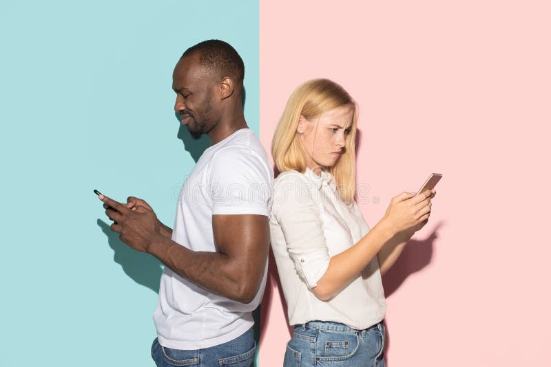 Coppie corse miste degli studenti che prendono i telefoni cellulari Ragazza caucasica e suo il ragazzo africano che posano allo s fotografia stock Coppie corse miste degli studenti che prendono i telefoni cellulari Ragazza caucasica e suo il ragazzo africano che posano allo s fotografia stock