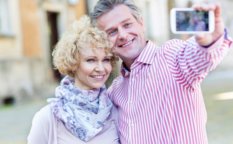 Coppie di mezza età felici che prendono selfie tramite lo Smart Phone all'aperto fotografia stock libera da diritti Coppie di mezza età felici che prendono selfie tramite lo Smart Phone all'aperto fotografia stock libera da diritti