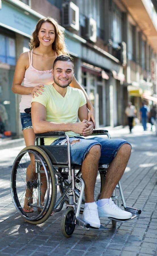 Coppie felici alla passeggiata della sedia a rotelle attraverso la città immagine stock Coppie felici alla passeggiata della sedia a rotelle attraverso la città immagine stock